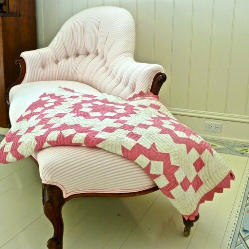 Antique chaise with pink ticking fabric and homemade quilt